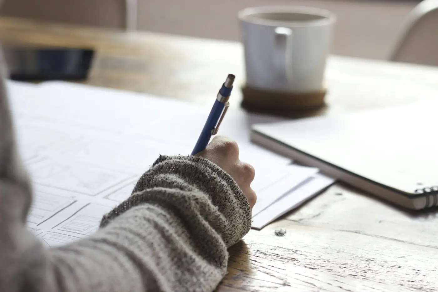 Person writing notes at a desk beside a coffee cup